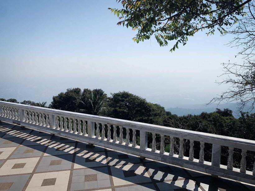 A terrace with a stone wall looking out onto trees and thick fog in the valley below