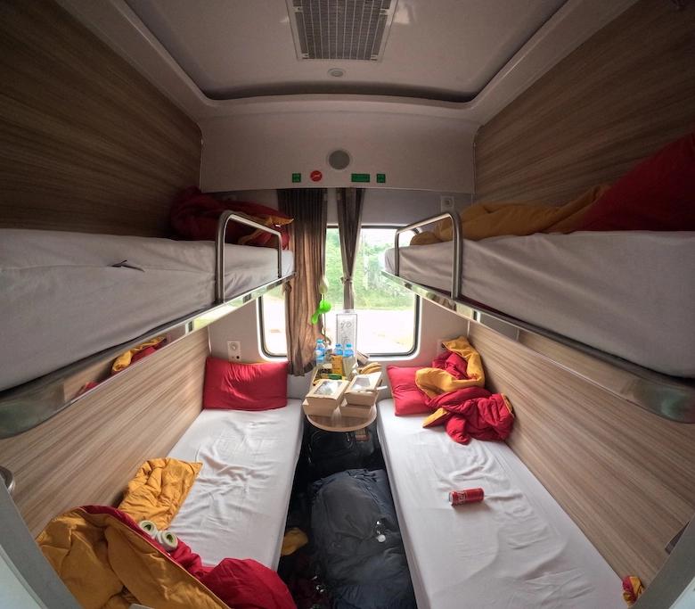 Interior of couchette of my train (the right one) from Ninh Binh to Huế, Vietnam. The couchette contains four bunk bed, with the beds unmade as the picutre is taken in the morning. In the middle it's possible to see a little window with some green plants outside. The window is partially covetrd by curtains