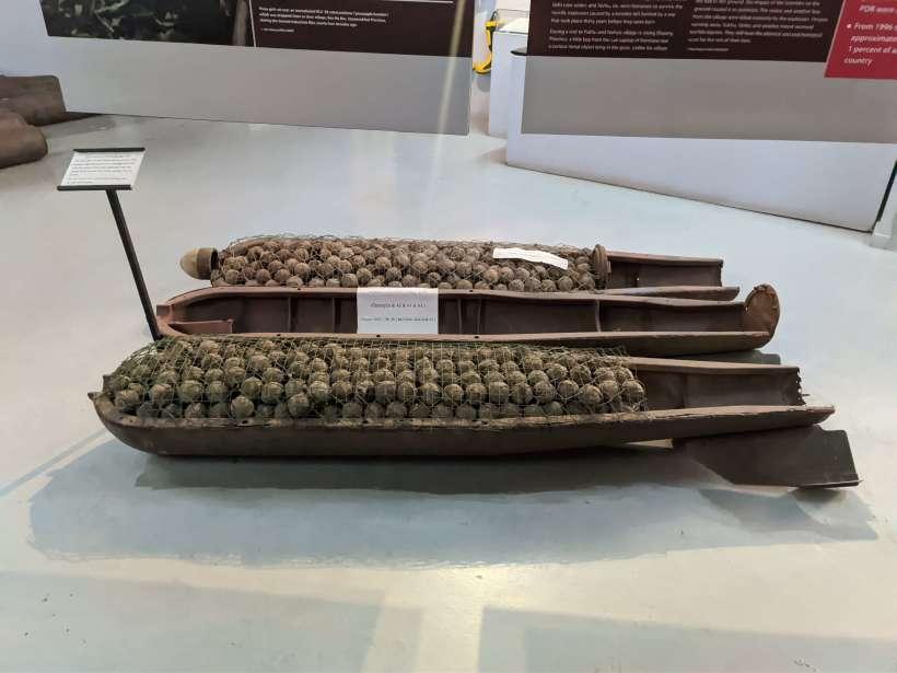 Inside of a cluster bomb full of bomblets, on display at the COPE museum in Luang Prabang. The bomb is open and you can see three parts. The left and the right ones are full of bomblets, while the middle part is empty, but it contains a sheet with something written on it. To the left of the bomb there is a pole with a white label on top that tells more abut details of the bombs.