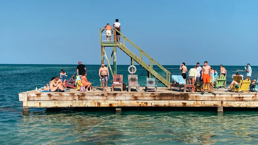 Pier at Lazy Lizard Pier seen from the side with people sitting on deckchairs and on diving board about to jump