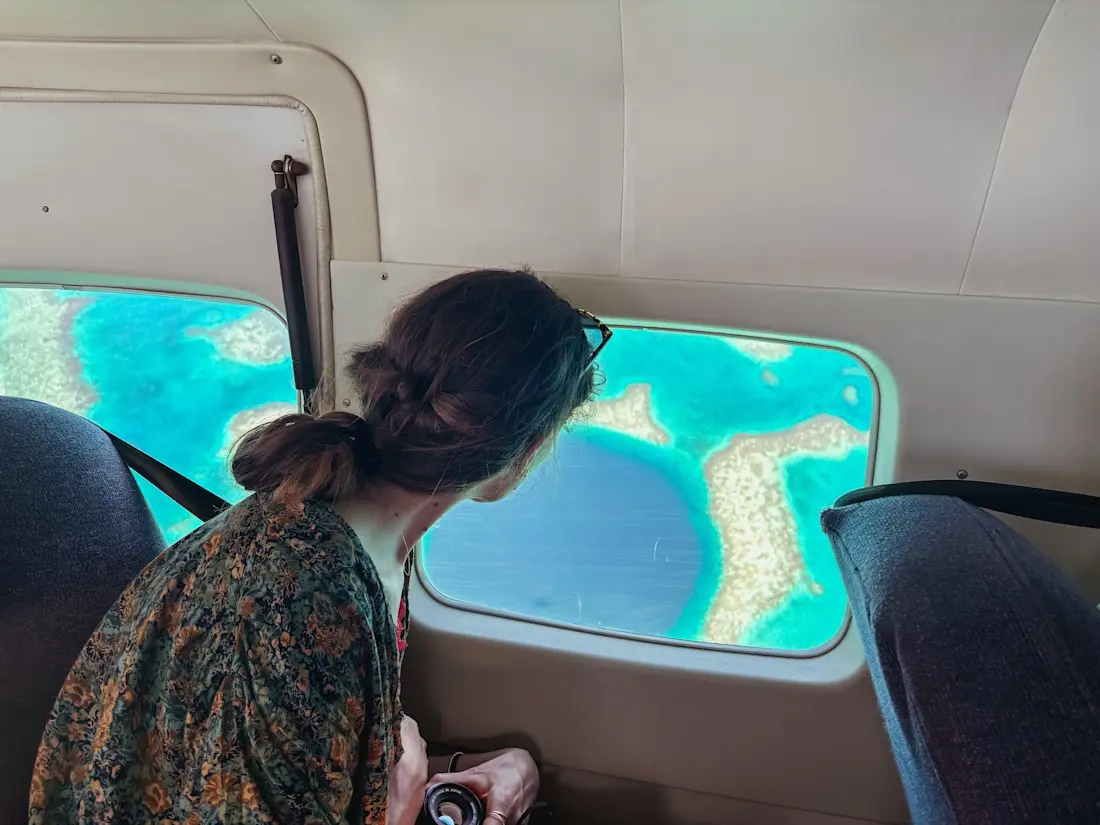 The Great Blue Hole Belize Central America Deep blue perfectly round sinkhole on a barrier reef seen from a window of a small airplane. A person with a camera in their hand is looking out of the window.