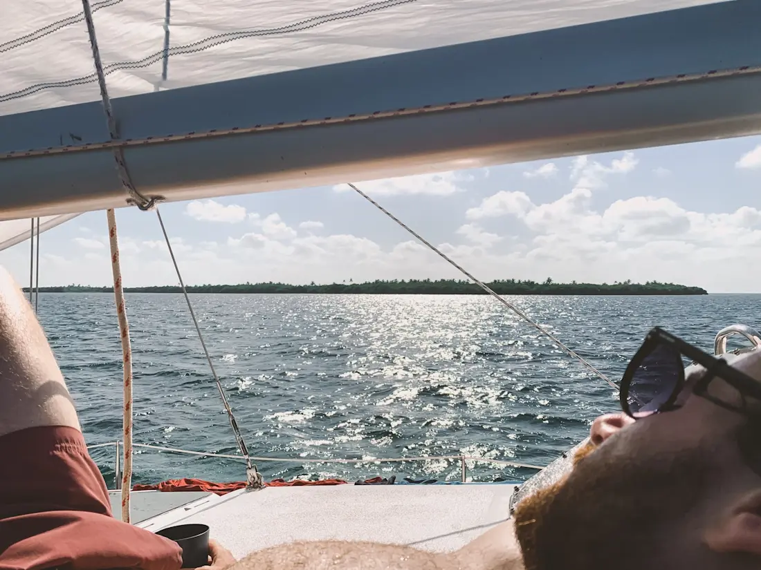 Davide relaxing on the sailing trip Person lying down on a sail boat looking towards a distant island with sails above him